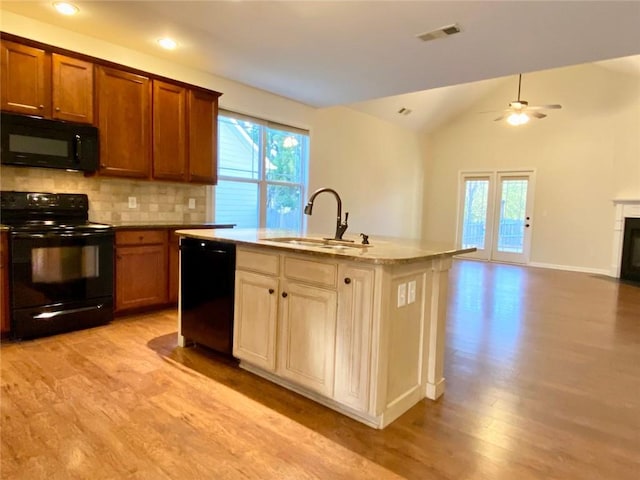 kitchen featuring backsplash, open floor plan, light wood-style floors, black appliances, and a sink