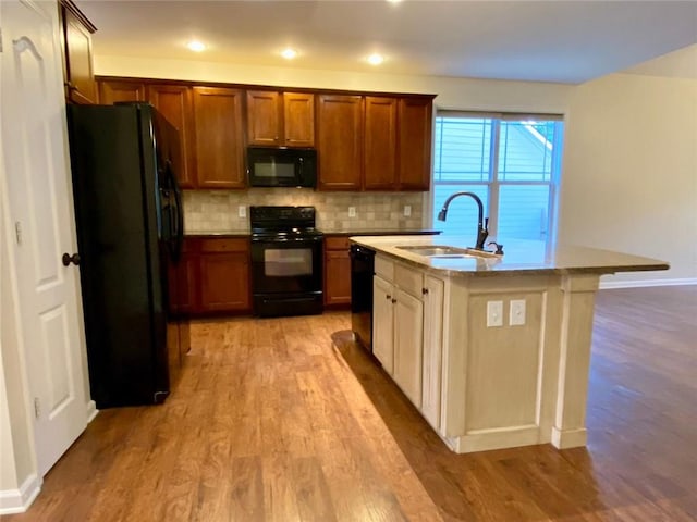 kitchen featuring a sink, decorative backsplash, black appliances, and light wood finished floors