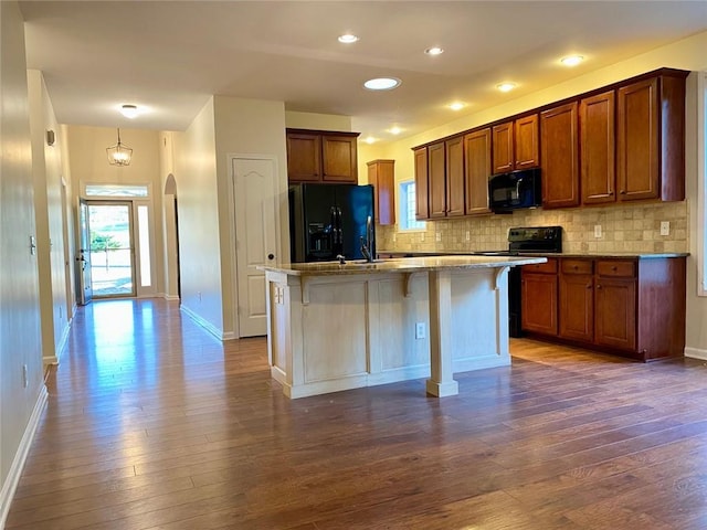 kitchen featuring decorative backsplash, black appliances, dark wood-type flooring, and a center island with sink