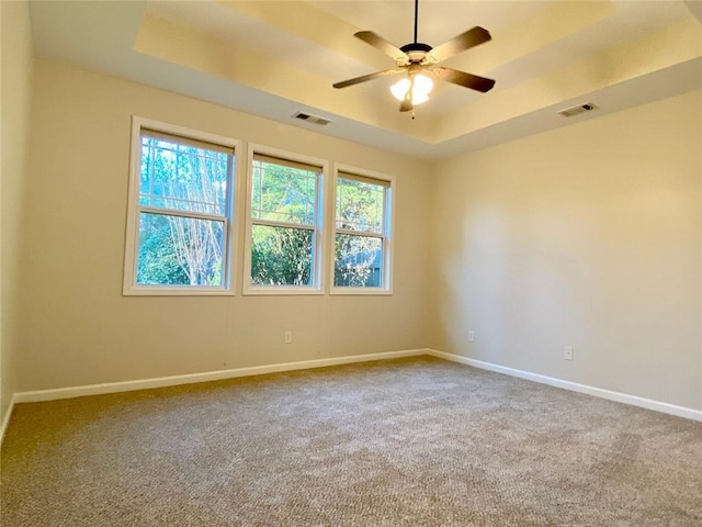 carpeted empty room with a raised ceiling, baseboards, visible vents, and ceiling fan