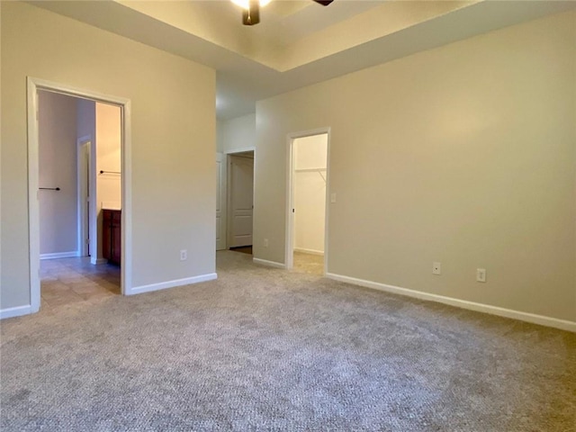 unfurnished bedroom featuring a walk in closet, a raised ceiling, baseboards, and carpet floors