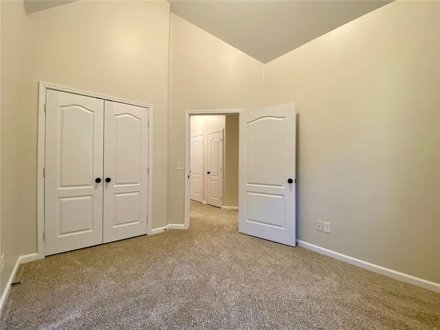 unfurnished bedroom featuring a closet, baseboards, high vaulted ceiling, and carpet flooring