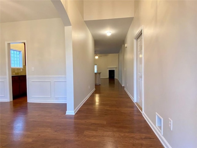 corridor with a wainscoted wall, visible vents, dark wood finished floors, arched walkways, and a decorative wall