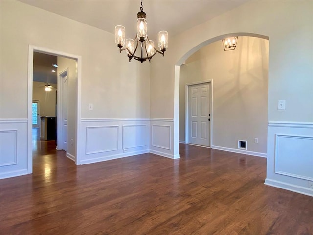 empty room featuring a decorative wall, visible vents, dark wood-style flooring, and a chandelier