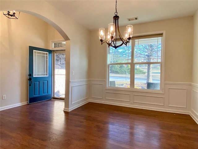 unfurnished dining area with visible vents, arched walkways, dark wood-style flooring, wainscoting, and a chandelier