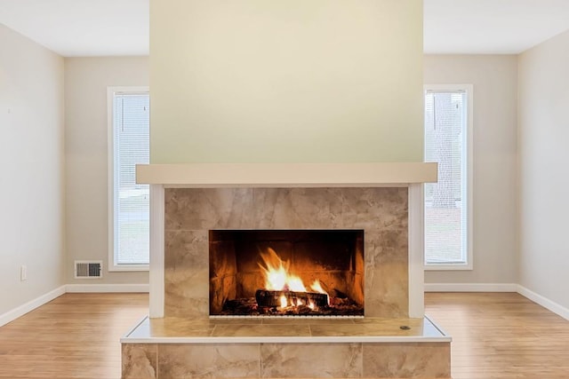 details with visible vents, baseboards, wood finished floors, and a tile fireplace