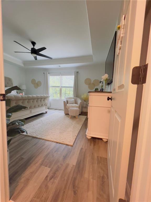 bedroom with ceiling fan, wood-type flooring, and a raised ceiling