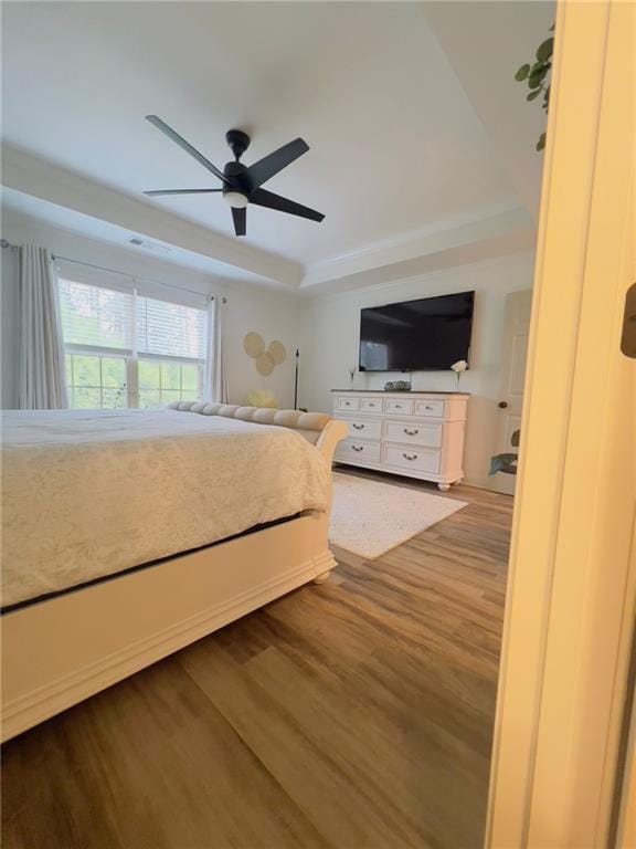 unfurnished bedroom featuring ceiling fan, wood-type flooring, and a raised ceiling