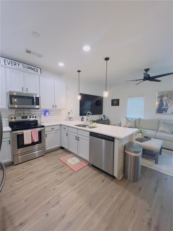 kitchen with white cabinetry, kitchen peninsula, stainless steel appliances, hanging light fixtures, and light hardwood / wood-style flooring