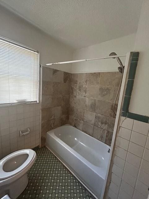 bathroom with tub / shower combination, toilet, tile walls, and a textured ceiling