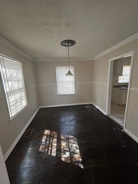 unfurnished dining area featuring a textured ceiling, crown molding, baseboards, and wood finished floors