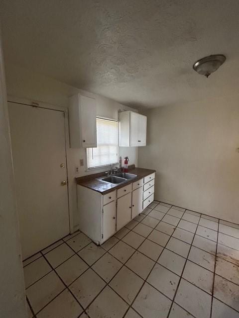 kitchen featuring dark countertops, light tile patterned flooring, white cabinets, a textured ceiling, and a sink