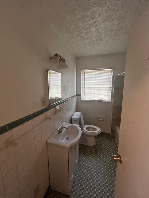 full bath featuring tile walls, a wainscoted wall, toilet, a textured ceiling, and vanity