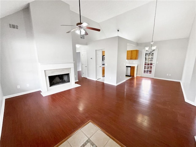 unfurnished living room featuring high vaulted ceiling, dark hardwood / wood-style floors, ceiling fan with notable chandelier, and a fireplace