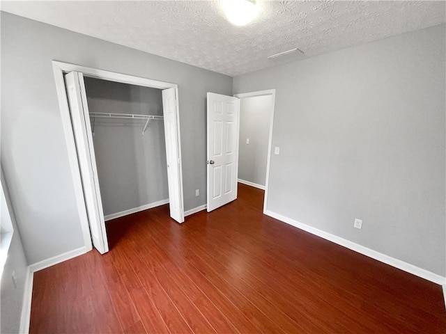 unfurnished bedroom featuring dark wood-type flooring, a closet, and a textured ceiling