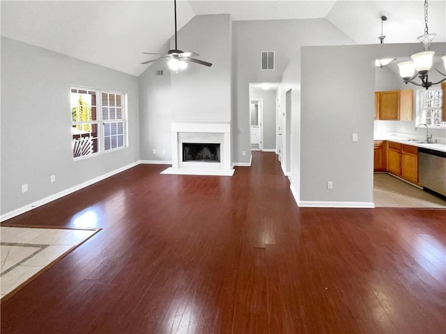 unfurnished living room with ceiling fan with notable chandelier, sink, hardwood / wood-style floors, and high vaulted ceiling