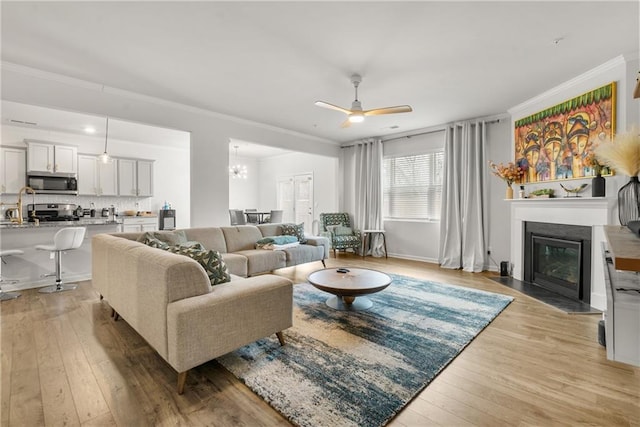 living room featuring light wood-type flooring, ceiling fan, ornamental molding, and sink