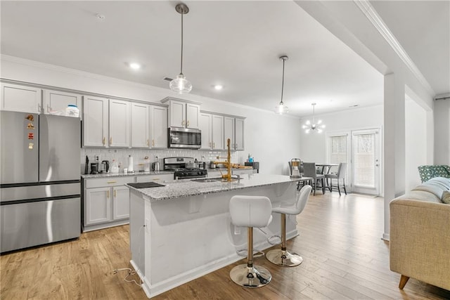 kitchen featuring a center island with sink, sink, hanging light fixtures, light stone countertops, and stainless steel appliances