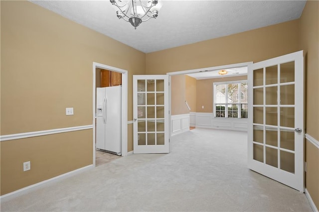 carpeted spare room featuring french doors, a textured ceiling, and an inviting chandelier