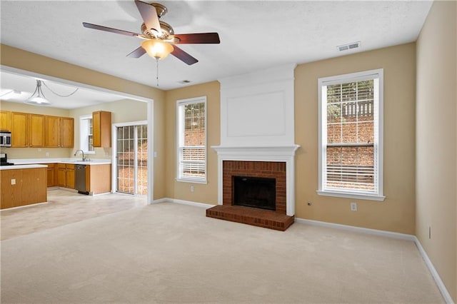 unfurnished living room with light carpet, sink, ceiling fan, and a brick fireplace