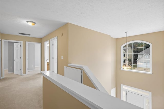 hallway featuring light carpet, a textured ceiling, and an inviting chandelier