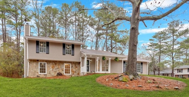 split level home with stone siding, a chimney, and a front lawn