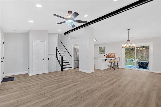 unfurnished living room featuring ceiling fan with notable chandelier, light wood-style floors, baseboards, vaulted ceiling with beams, and stairs