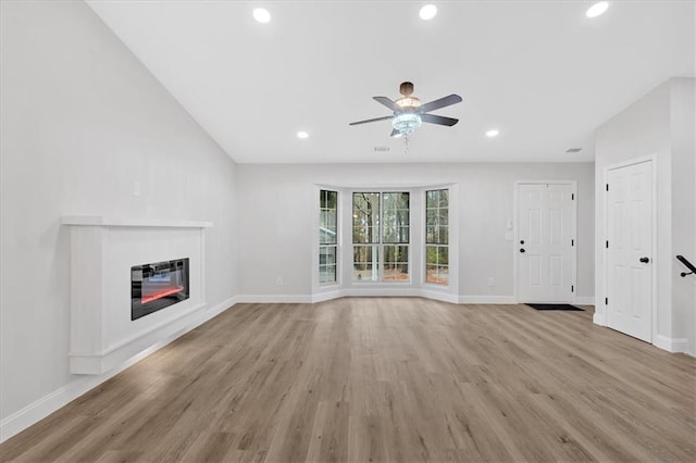 unfurnished living room with a glass covered fireplace, light wood-style flooring, recessed lighting, and baseboards