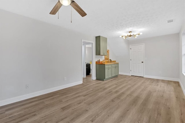 unfurnished living room with visible vents, ceiling fan with notable chandelier, a textured ceiling, light wood finished floors, and baseboards