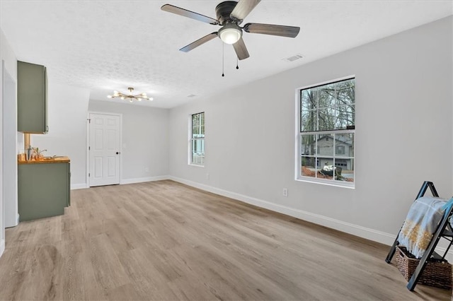 unfurnished living room with light wood-style flooring, baseboards, visible vents, and a textured ceiling