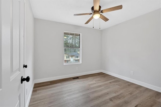 spare room with ceiling fan, visible vents, baseboards, and wood finished floors