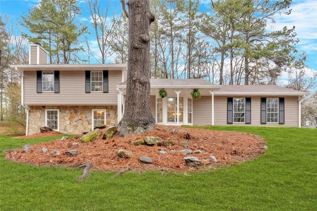 split level home featuring stone siding, a chimney, and a front yard