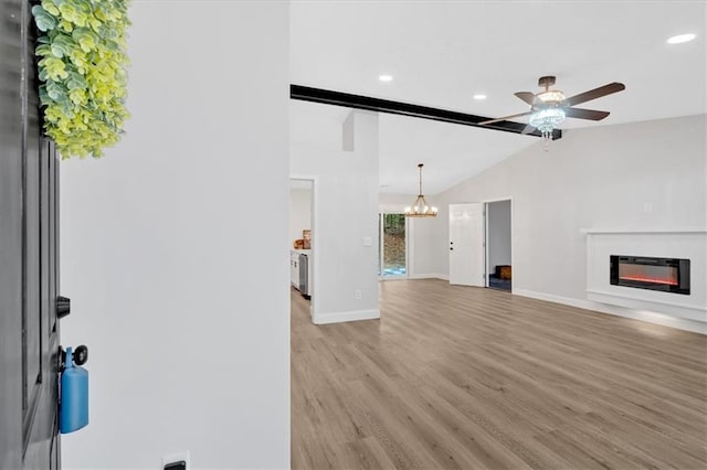 unfurnished living room featuring baseboards, vaulted ceiling, light wood-style flooring, ceiling fan with notable chandelier, and a glass covered fireplace