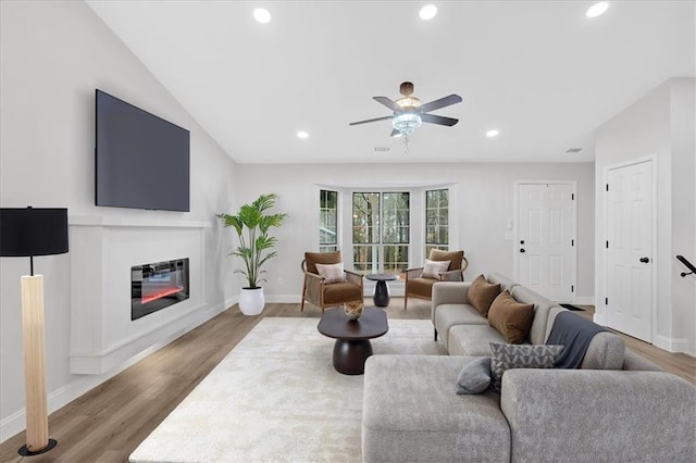 living room featuring a glass covered fireplace, lofted ceiling, recessed lighting, and wood finished floors