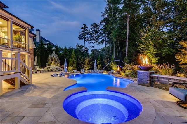 pool at dusk featuring pool water feature, an in ground hot tub, and a patio