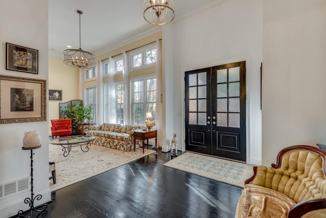 foyer entrance with french doors, crown molding, a towering ceiling, wood-type flooring, and a chandelier