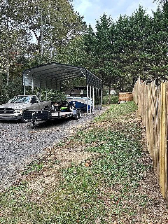 view of parking with fence, a carport, and gravel driveway
