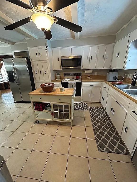kitchen featuring appliances with stainless steel finishes, beam ceiling, light tile patterned floors, a sink, and white cabinets