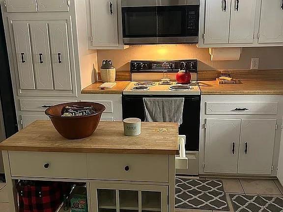 kitchen with white cabinets, light tile patterned flooring, electric range oven, light countertops, and stainless steel microwave