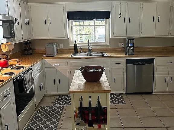 kitchen with a sink, appliances with stainless steel finishes, light tile patterned floors, and white cabinets