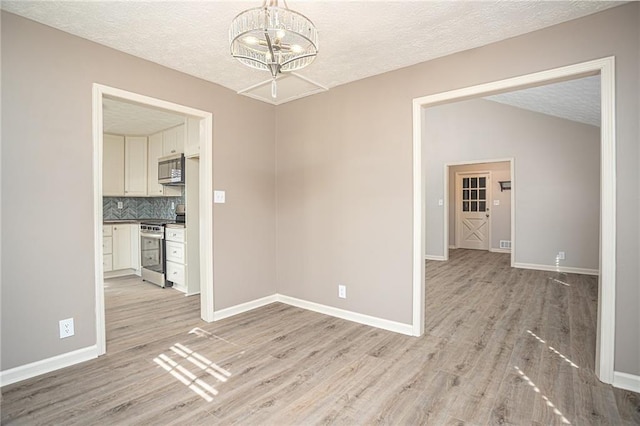 1312 La Mesa Dr, Lawrenceville, GA 30043 - unfurnished dining area featuring light wood-style flooring, a chandelier, a textured ceiling, baseboards, and lofted ceiling