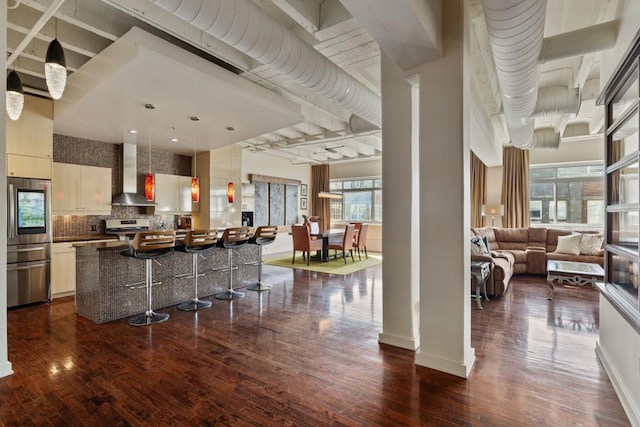 kitchen featuring wall chimney exhaust hood, a breakfast bar, open floor plan, a center island, and hanging light fixtures