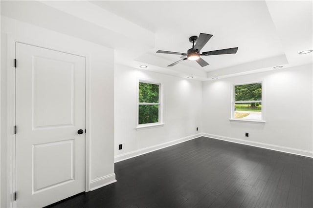 unfurnished room featuring a raised ceiling, ceiling fan, and dark wood-type flooring