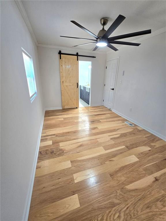 empty room with baseboards, crown molding, light wood finished floors, and a barn door