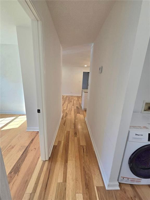 corridor featuring light wood-type flooring, baseboards, and washer / clothes dryer