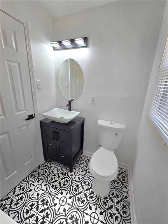 half bathroom featuring toilet, tile patterned flooring, baseboards, and vanity