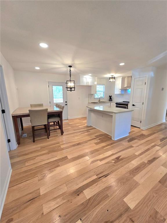 kitchen featuring white cabinets, light countertops, light wood-type flooring, wall chimney exhaust hood, and plenty of natural light