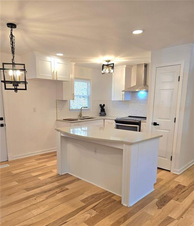 kitchen featuring electric range, white cabinets, wall chimney range hood, and light wood finished floors