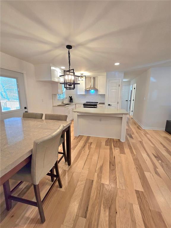 kitchen with stainless steel stove, decorative backsplash, light wood-style floors, white cabinets, and wall chimney range hood
