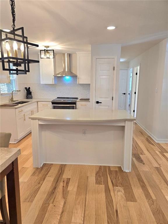 kitchen featuring a sink, white cabinetry, decorative backsplash, stainless steel electric range oven, and wall chimney exhaust hood